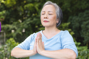 Practicing yoga outdoors, senior Asian female wearing a light blue top