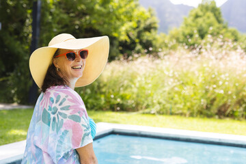 Outdoors, Caucasian senior female wearing sunglasses, smiling by pool, copy space