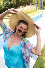 Outdoors, Caucasian senior woman wearing a large hat and sunglasses by poolside