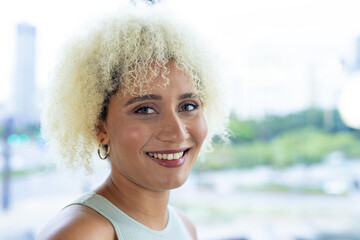 In modern office, a young biracial woman with curly blonde hair smiling