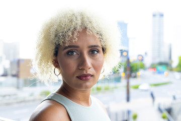 Young biracial woman with blonde curls and brown eyes looks ahead in modern office - Powered by Adobe