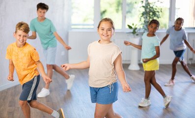 Dynamic little girl training Rock-and-Roll dance poses in dancehall with other attendees of dancing...