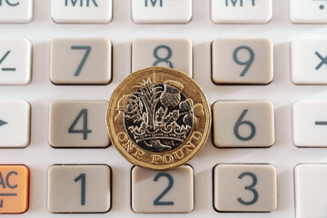 British one pound coin placed on top of the calculator buttons. Concept for business, planning and finance