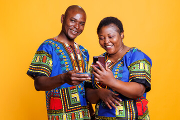 African american couple wearing ethnic clothes paying online using mobile phone. Husband holding debit card and looking at camera while wife scrolling internet store on smartphone