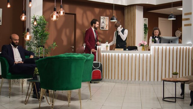 Businessman begins registration process by discussing with hotel staff at front desk reception. Executive manager is eager to visit the venue and prepare for upcoming global conference.