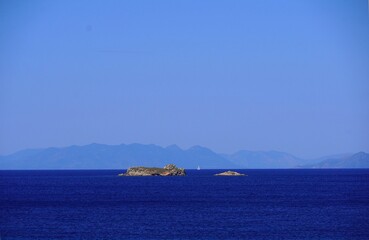 A white sailboat between two small islands, near the coast of Attica, Greece