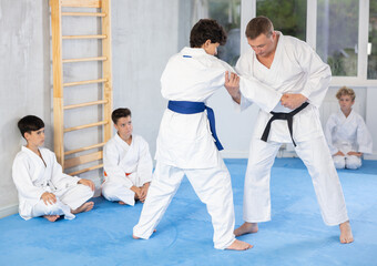 Male karate instructor training little child wearing kimono in dojo or jiu-jitsu in gym at tatami