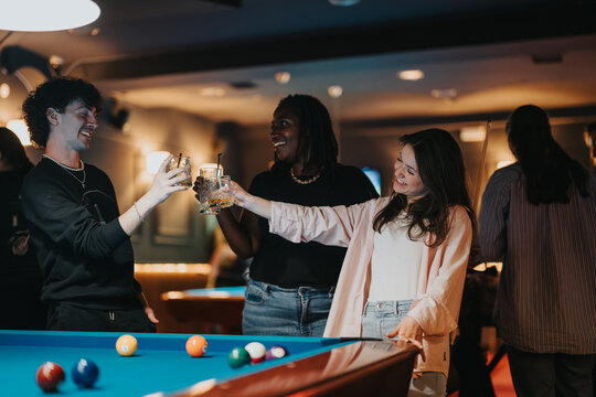 A joyful gathering of friends enjoying drinks and playing pool in a cozy bar atmosphere at night.