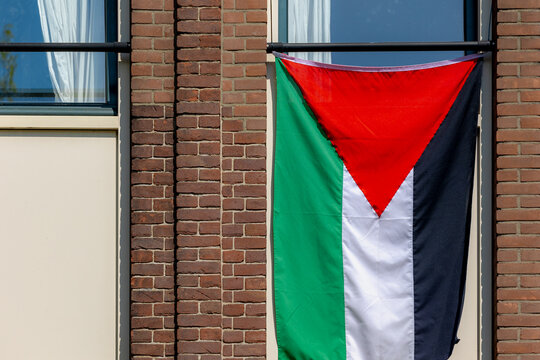 The flag of Palestine hanging outside the window of building, Tricolor of three equal horizontal stripes (black, white, and green with a red triangle) overlaid by a red triangle issuing from the hoist