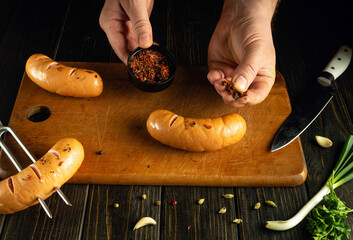 Cooking juicy sausages with spices by the hands of a chef on the kitchen table before lunch.