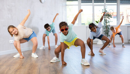 Obraz premium Positive juvenile girl engaged in Breakdancing together with children's group in training room during workout session