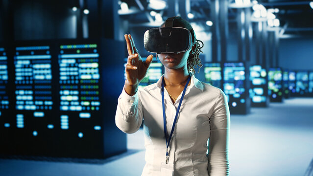 African american woman immersed in virtual reality at data center, doing equipment maintenance. Qualified engineer using VR headset to optimize server equipment performance, checking operations