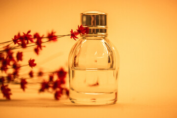 Single transparent glass perfume bottle on yellow background. Bouquet of small beautiful red...