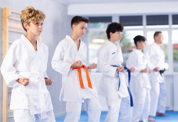 Concentrated teenager in white kimono practicing punches in gym during group martial arts workout....