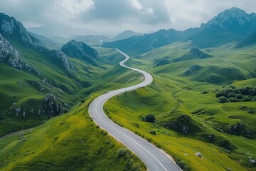 Birds-eye view of a winding road through lush green rolling hills under a cloudy sky