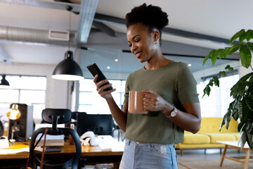 At office, African American businesswoman holding coffee, looking at phone
