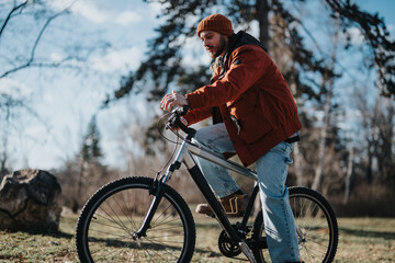 Obraz premium Casual bearded man enjoying free time in nature, leaning on his bicycle outdoors in a park setting.