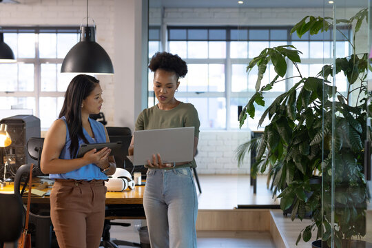 At office, diverse female business colleagues holding laptop, discussing work