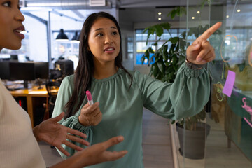 At office, diverse female business colleagues discussing at glass board