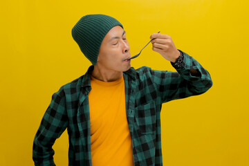 A contemplative Asian man, dressed in a beanie hat and casual shirt, relishes a delightful meal,...