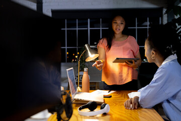 Diverse female colleagues discussing work on tablet, working late