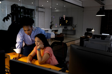 Diverse female business colleagues discussing over computer, working late
