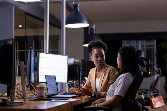 Working late, diverse female colleagues discussing work
