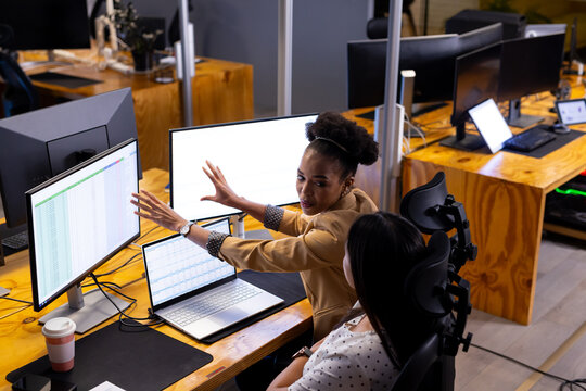 Diverse female colleagues at office discuss spreadsheets, working late