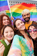 Happy vertical selfie of a group of LGBTQIA people in the pride day, looking at camera cheerfully holding rainbow flags. Concept of Supporting the Homosexual community.