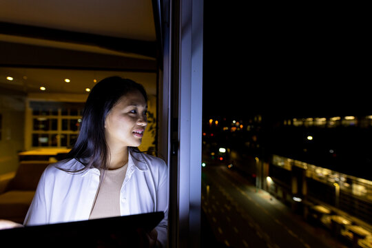 At office, biracial businesswoman studying tablet near a window at night, copy space