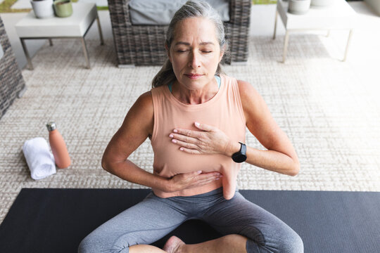 At home, mature Caucasian woman sitting cross-legged, practicing yoga