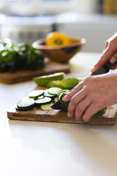 At home, mature Caucasian woman slicing zucchini on a wooden board