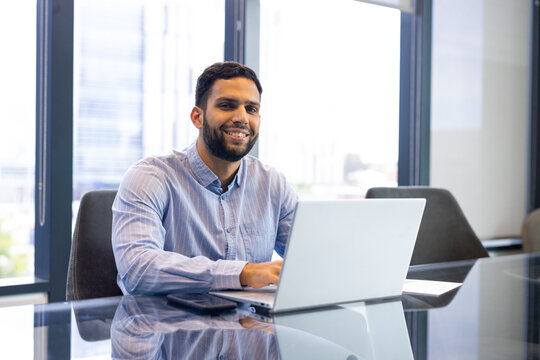 A biracial young professional man, sitting at office desk, typing on laptop