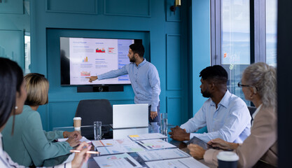A diverse team at office, including biracial man in blue shirt, pointing at a screen