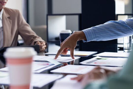 Diverse team reviewing business papers at office, senior professional pointing