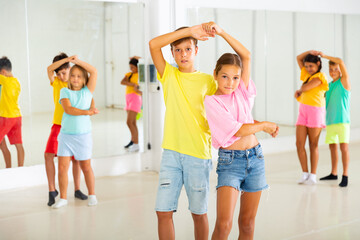 Positive preteen children learning to dance waltz in pairs in choreography class.