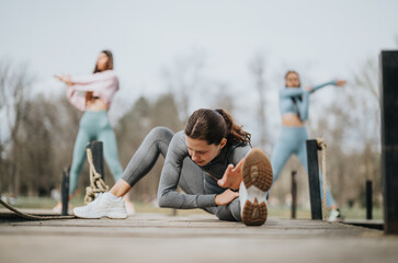 Group of women engaging in stretching exercises at a park, showcasing strength, flexibility, and...