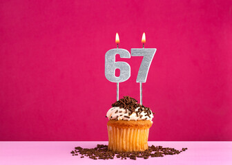 Birthday celebration with candle number 67 - Chocolate cupcake on pink background