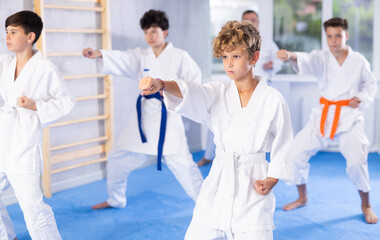 Diligent preteen attendee of karate classes practicing kata standing in row with others in sports...