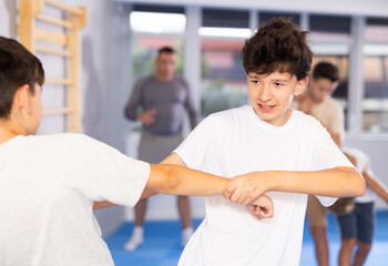 Willing junior attendee of self-defense classes fighting with his opponent in sports hall