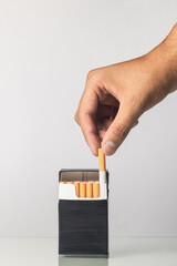 Latin man's hand grabbing a cigarette in a black package with white background.