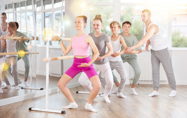 Gracious teen girl doing plie position being controlled by instructor during ballet courses