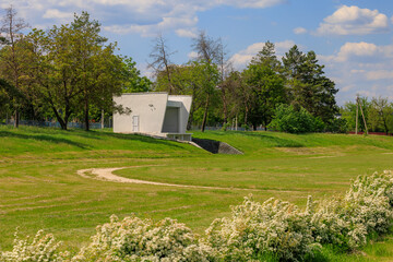 A white building sits in a grassy field with trees in the background