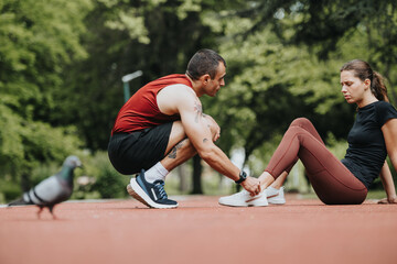 A fit man provides aid to his girlfriend who has hurt her leg while jogging in a serene park...