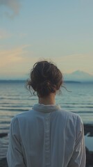 Fototapeta premium Woman white shirt stands shoreline dusk looking peaceful ocean distant clouds
