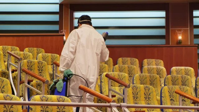 Antivirus fog sanitation in theater, man in uniform of chemical protective disinfecting surface of chairs with Fumigation Fogger Disinfection Machine