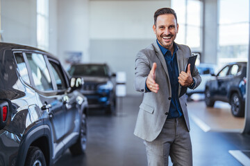 Good looking, cheerful and friendly salesman poses in a car salon or showroom and looks at camera....