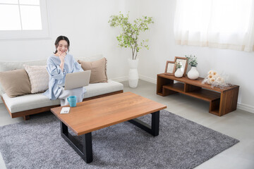Woman using a computer sitting in the living room Image of a woman working remotely or at home Looking at a computer, searching and thinking Full body
