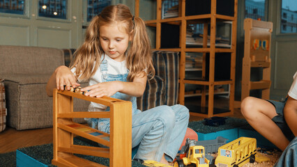 Caucasian girl sits at sand box while placed car model at slope toy. Diverse children playing...