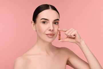 Beautiful young woman holding skincare ampoule on pink background